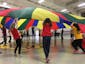 Kids playing with a multicolored parachute at school in a gymnasium
